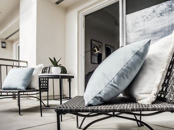 A black wicker chair with a grey cushion is in the foreground of a bright room.